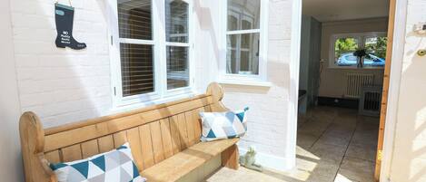 A wooden bench with cushions, a white brick wall, and a window with shutters.