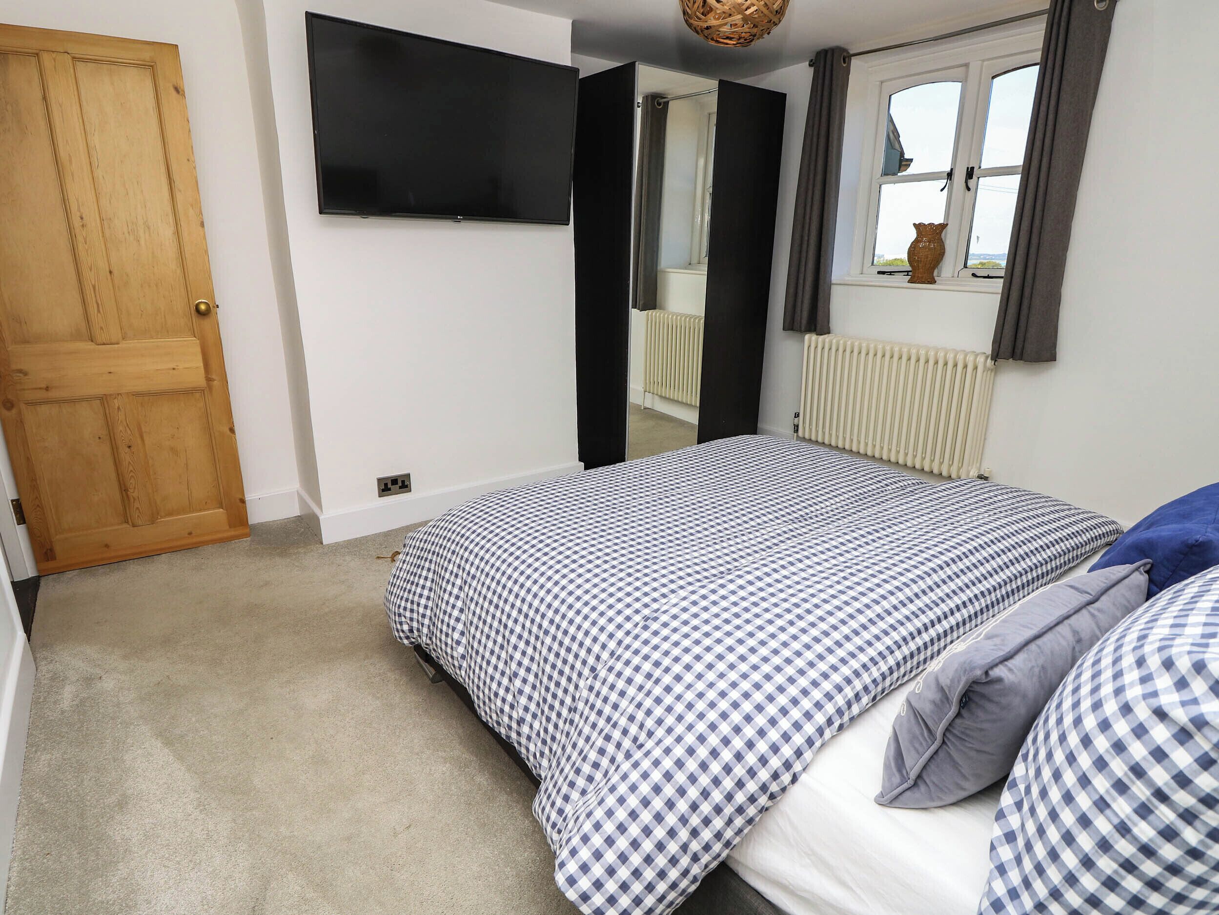 A bedroom with a bed, a television mounted on the wall, a window with curtains, and a radiator.