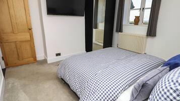 A bedroom with a bed, a television mounted on the wall, a window with curtains, and a radiator.