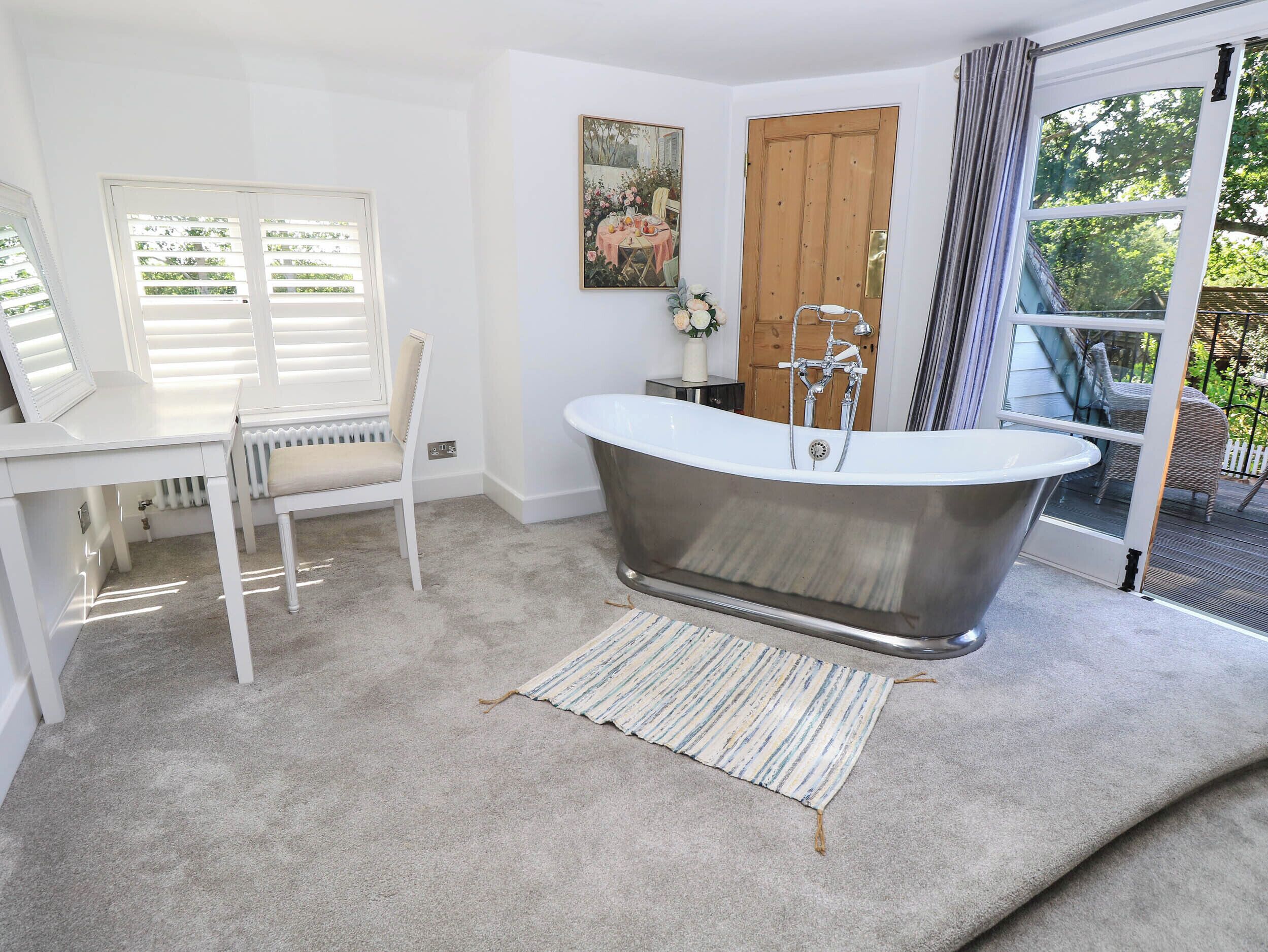 A bathroom with a freestanding bathtub, a white radiator, a chair, and a window with blinds.