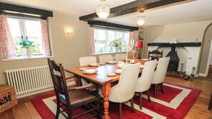 Comedor con una mesa de madera dispuesta para seis personas, rodeada de seis sillas, un tapete rojo y blanco, y una chimenea al fondo.
