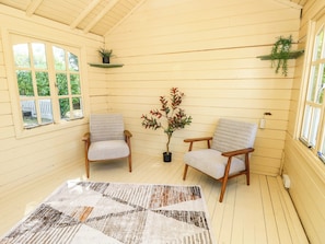 A room with two wooden chairs, a patterned rug, a potted plant, and a window with a view of greenery.