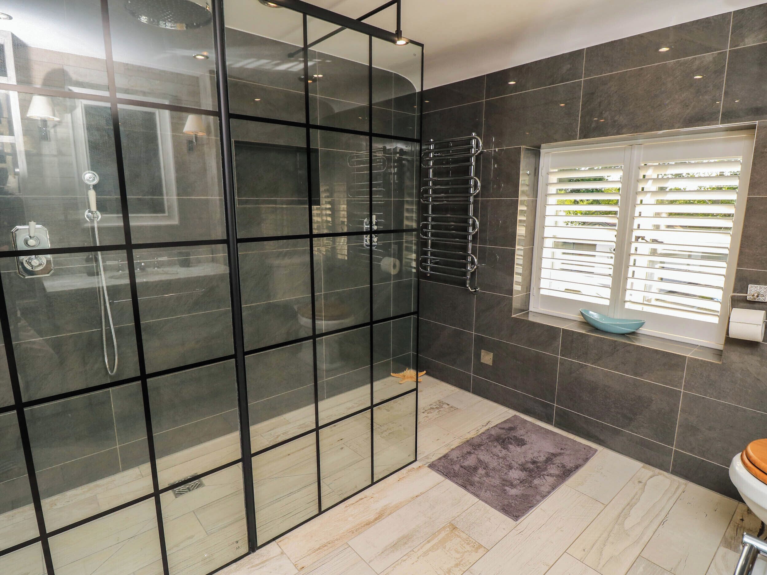 A modern bathroom with a glass shower enclosure, a towel rack, a window with blinds, and a toilet.