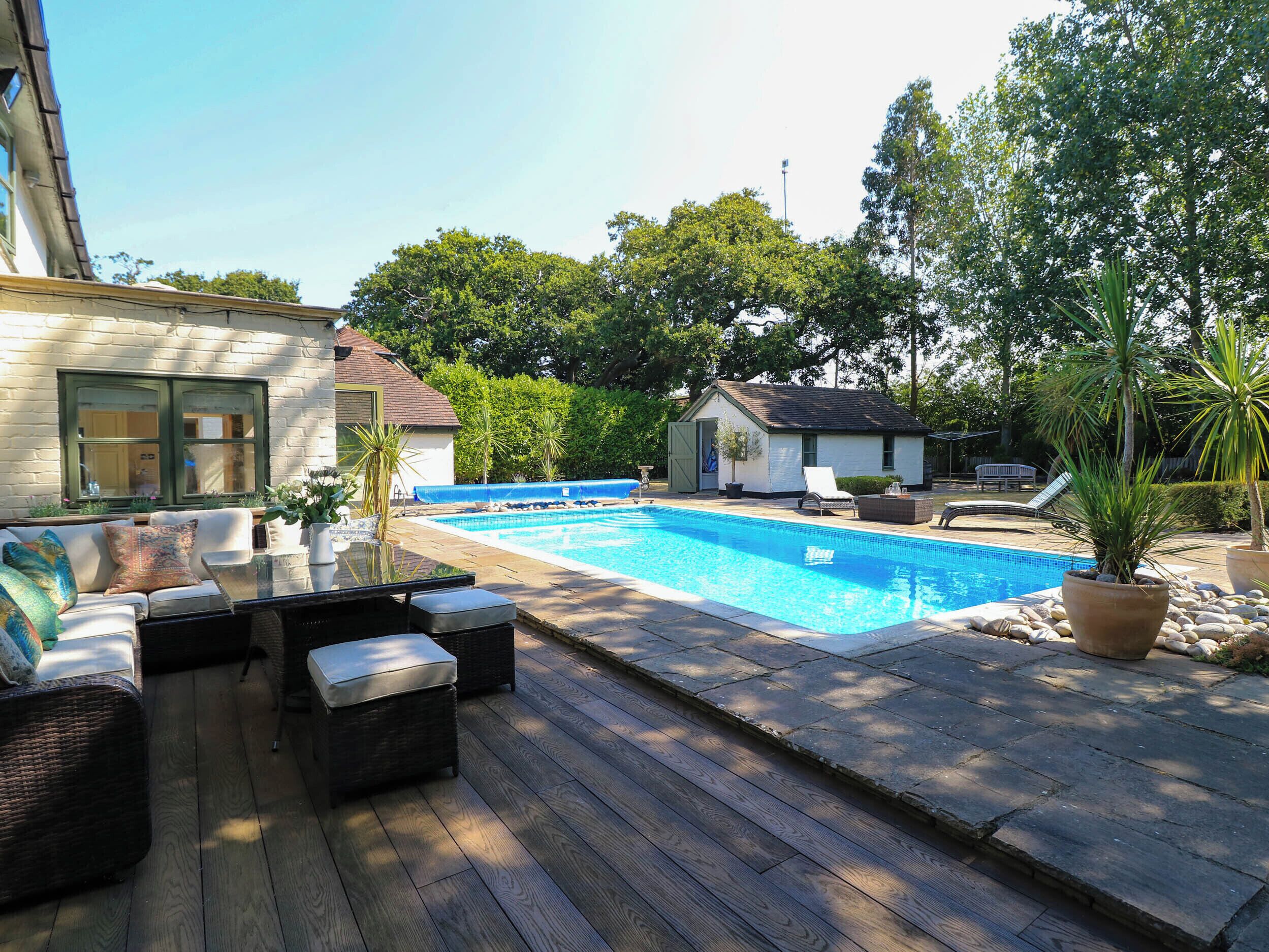 A swimming pool with a deck, lounge chairs, and a small building in the background.
