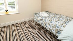 Un dormitorio con una cama individual, una ventana con persianas, un suelo a rayas y una pequeña figurita en el alféizar.