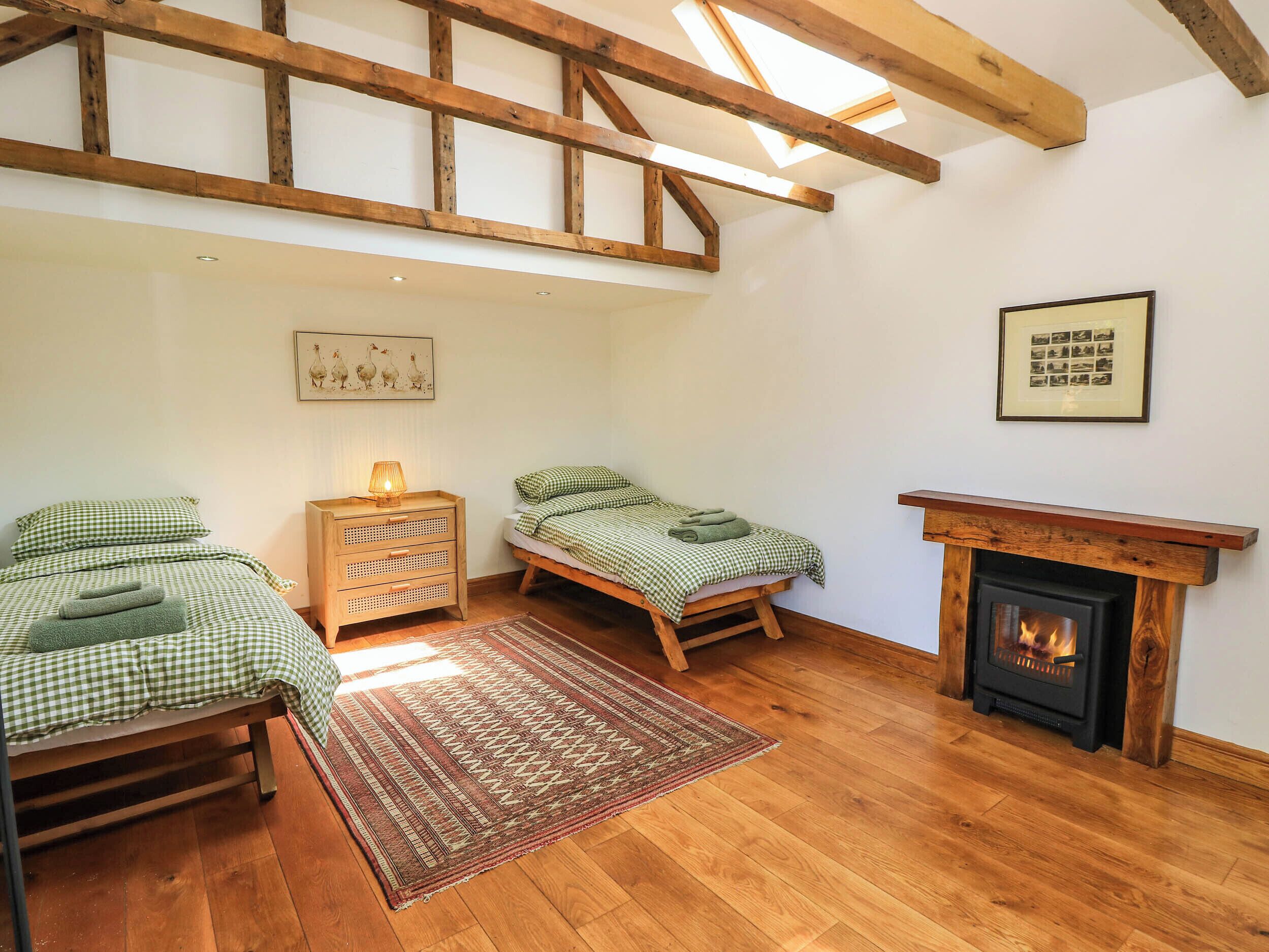 A cozy room with two beds, a wooden floor, a fireplace, and a skylight.