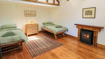 A cozy room with two beds, a wooden floor, a fireplace, and a skylight.