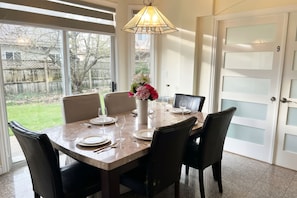 A dining area with a table set for four, chairs, a vase with flowers, and a hanging light fixture. - Two Bedrooms/4 Guests 15 Min YVR, A/C (Richmond)
