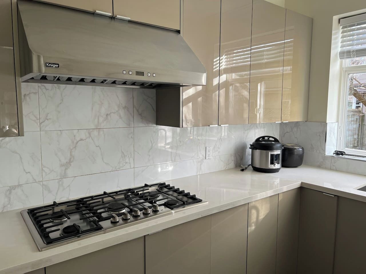 Una cocina moderna con estufa a gas, campana extractora de acero inoxidable y ventana con persianas.