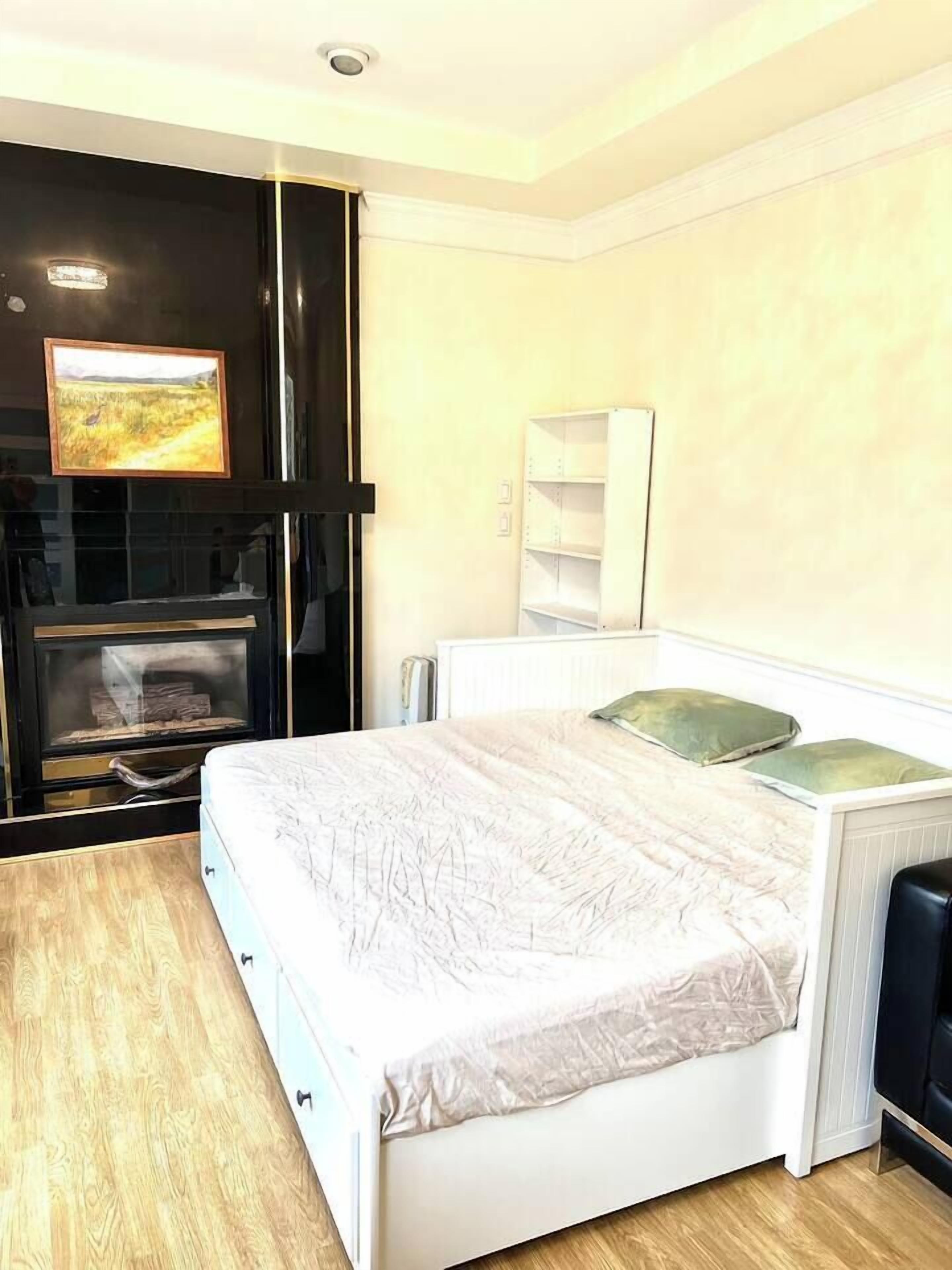 A bedroom with a bed, a built-in TV, a radiator, and a wooden floor.