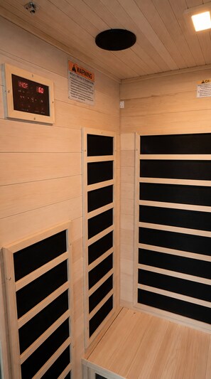 Una sauna amb parets de fusta, un termòmetre digital i un senyal de precaució.