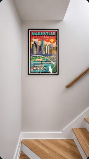 A framed cityscape poster of Nashville, Tennessee, hanging on a white wall above a wooden staircase. - East Nashville Wellness Stay: Sauna | Gym| Rooftop (Nashville)