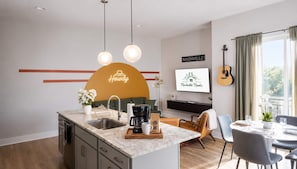 A modern kitchen with a central island, a dining area with a table set for two, and a living space with a guitar and a TV displaying 'Nashville Nooks'. - East Nashville Wellness Stay: Sauna | Gym| Rooftop (Nashville)