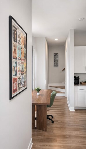 Une cuisine moderne avec des meubles blancs, une table à manger en bois et une affiche encadrée accrochée au mur.