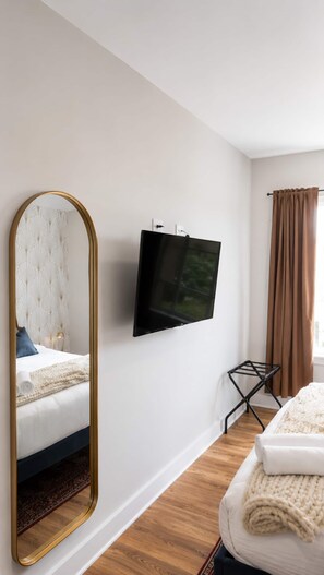 Une chambre d’hôtel avec un lit, un grand miroir, un téléviseur à écran plat, une fenêtre avec des rideaux et un plancher en bois.