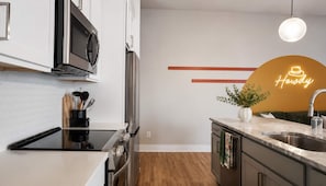 A modern kitchen with stainless steel appliances, a wooden floor, and a neon sign on the wall. - East Nashville Wellness Stay: Sauna | Gym| Rooftop (Nashville)