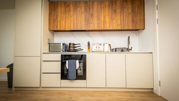 A compact kitchen with wooden cabinets, a microwave, a stove, and a small oven.