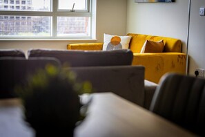 A living room with a sofa and armchairs, a window with a view of buildings, and a wall-mounted shelf. - Birmingham City Retreat No 146 (Birmingham)