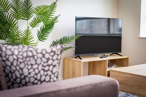 A modern living room with a flat-screen TV on a wooden stand, a patterned sofa, and a large green plant. - Birmingham City Retreat No 146 (Birmingham)