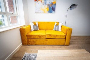 Ein gelbes Sofa mit zwei Kissen, eine moderne Stehlampe und ein Bild an der Wand.