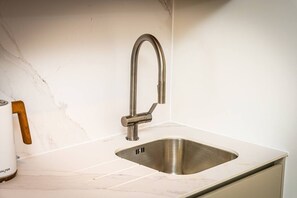 A kitchen with a stainless steel sink, a wooden-handled mug, and a marble backsplash. - Birmingham City Retreat No 146 (Birmingham)