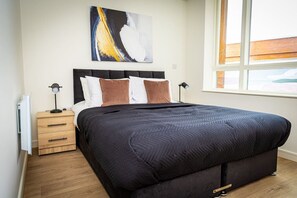 A bedroom with a bed, bedside tables, a lamp, a painting, and a window. - Birmingham City Retreat No 146 (Birmingham)
