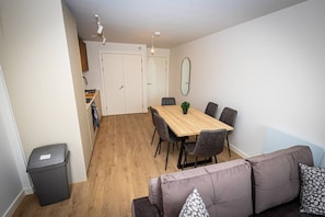 A compact living space with a dining area, a sofa, a trash bin, and a kitchen area with a bicycle. - Birmingham City Retreat No 146 (Birmingham)