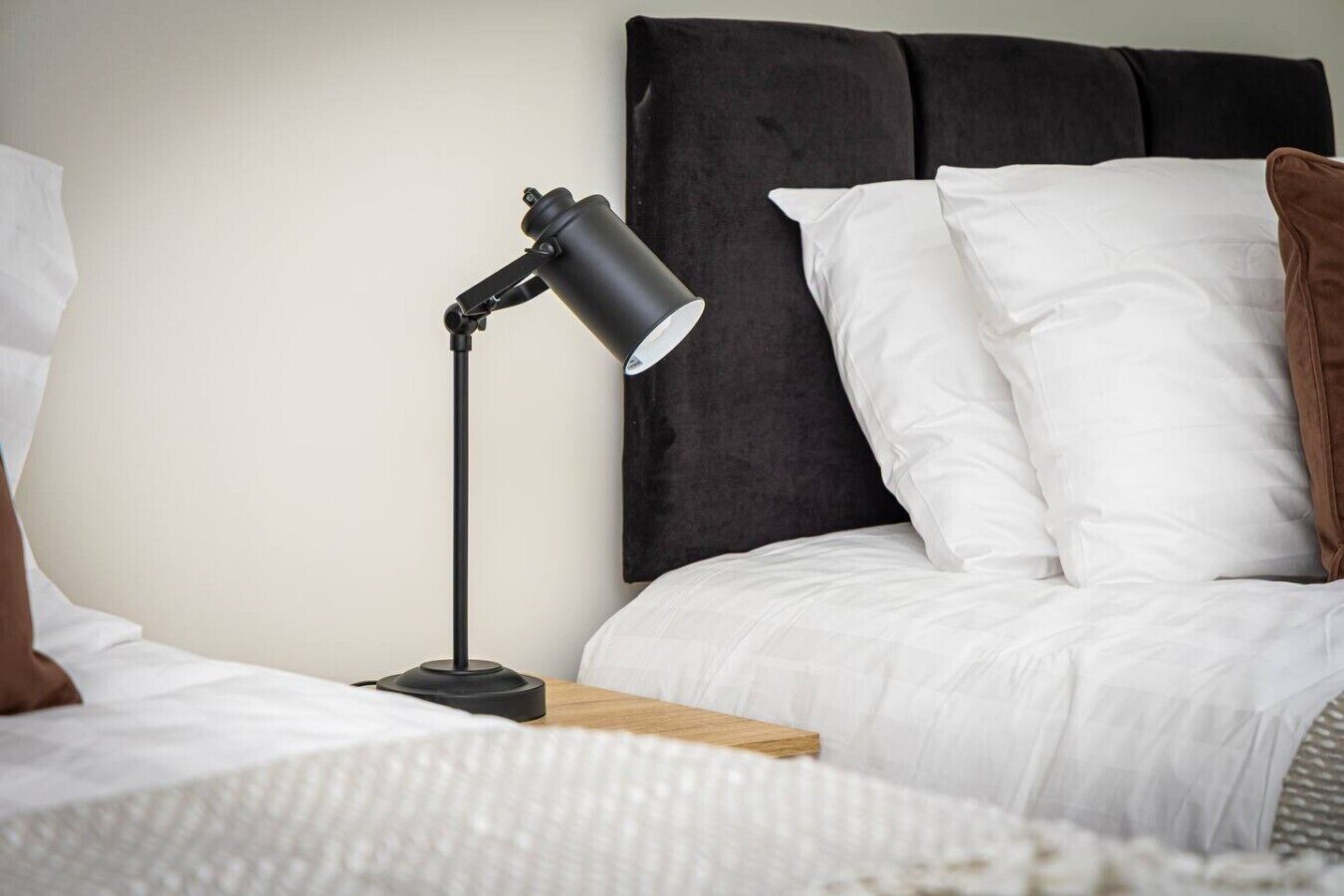 A neatly made bed with white bedding, a black nightstand, and a black desk lamp.