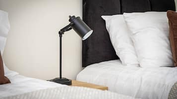 A neatly made bed with white bedding, a black nightstand, and a black desk lamp.