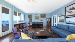 A living room with a large window, a dining area, and a blue sofa. - Penthouse 4BR Apartment · Terrace · Bosphorus View · Central Beyoğlu (Beyoğlu)