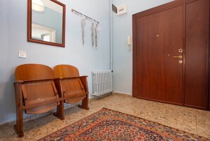 Une pièce avec une armoire en bois, un radiateur, un tapis à motifs et deux chaises en bois.