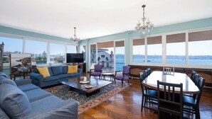 A spacious living room with a large window, a sofa set, a dining table, and a chandelier. - Penthouse 4BR Apartment · Terrace · Bosphorus View · Central Beyoğlu (Beyoğlu)