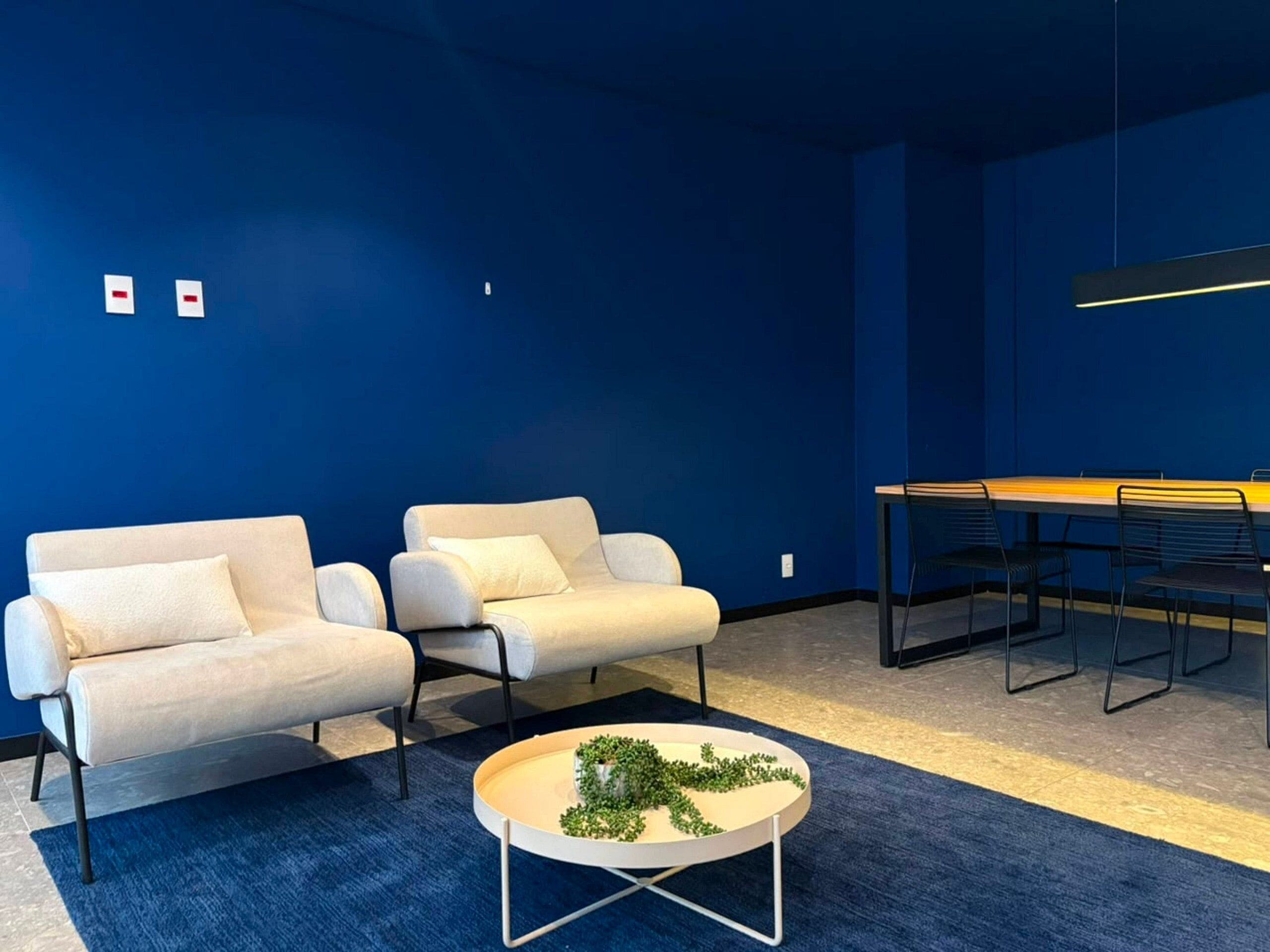 Une pièce moderne avec deux canapés beiges, une petite table basse ronde ornée d’une plante, et une table à manger avec des chaises.