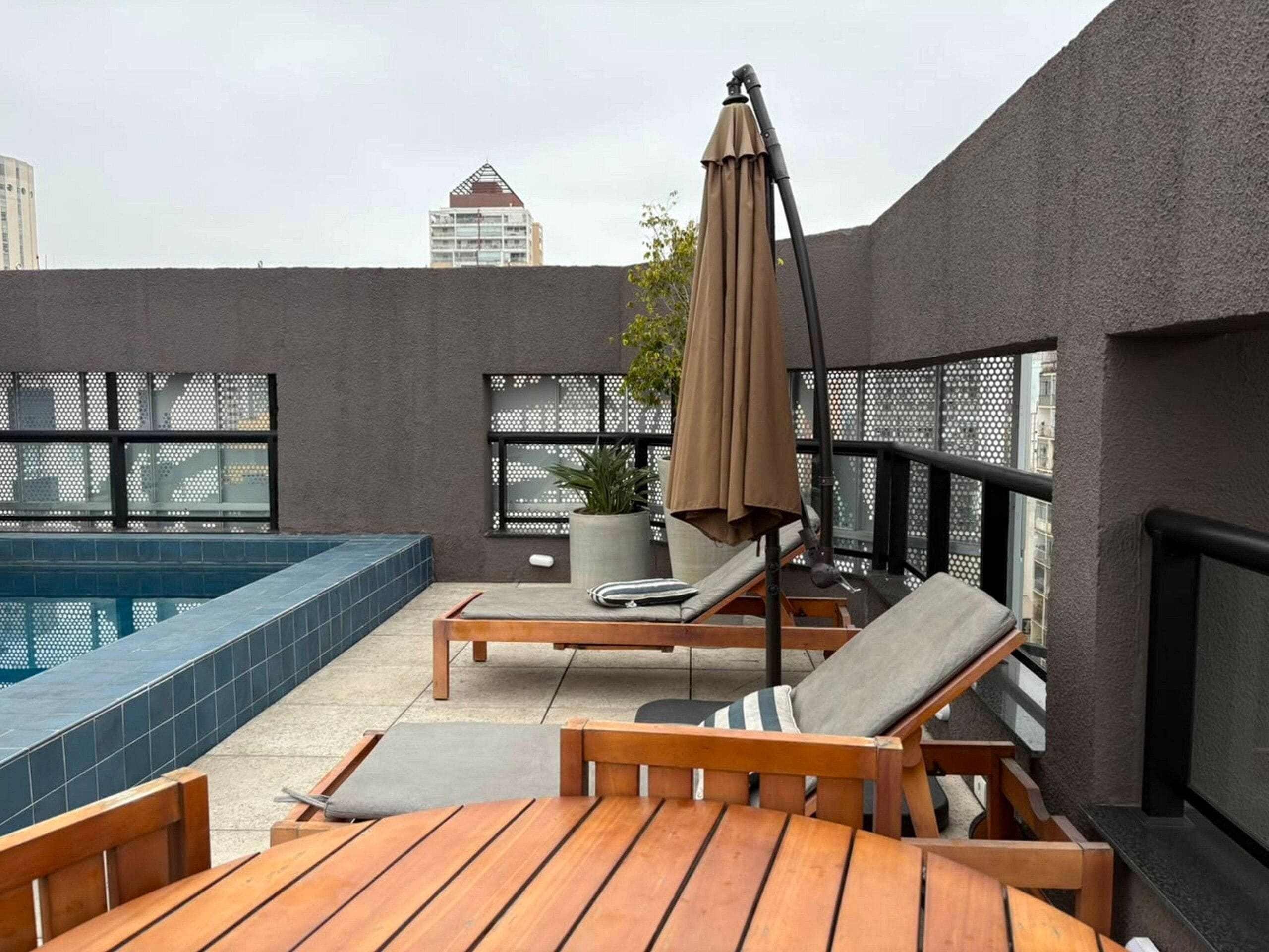 En tagterrasse med swimmingpool, liggestole og en potteplante.