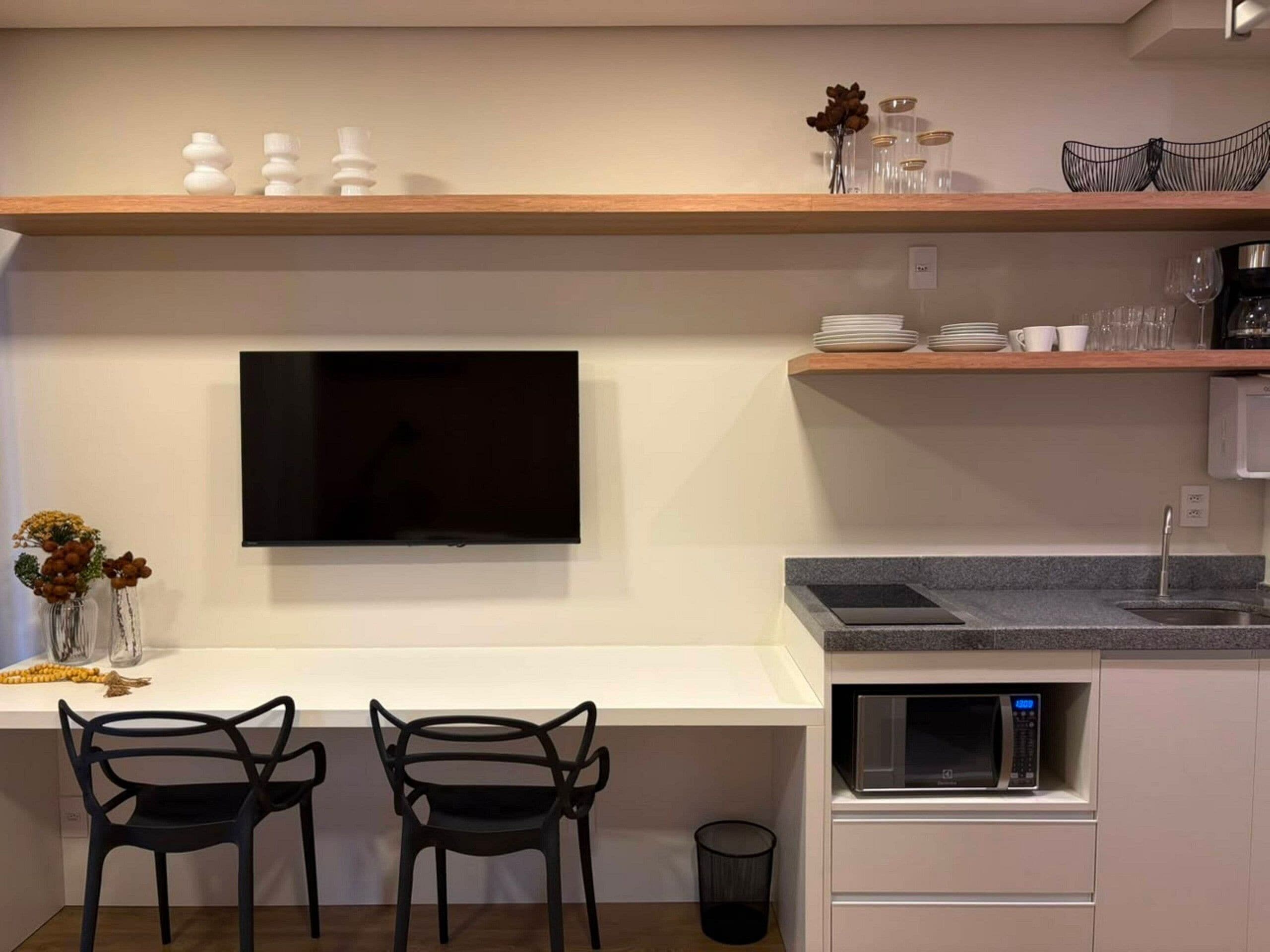 A modern kitchen with a flat-screen TV, two chairs, a microwave, and a sink.