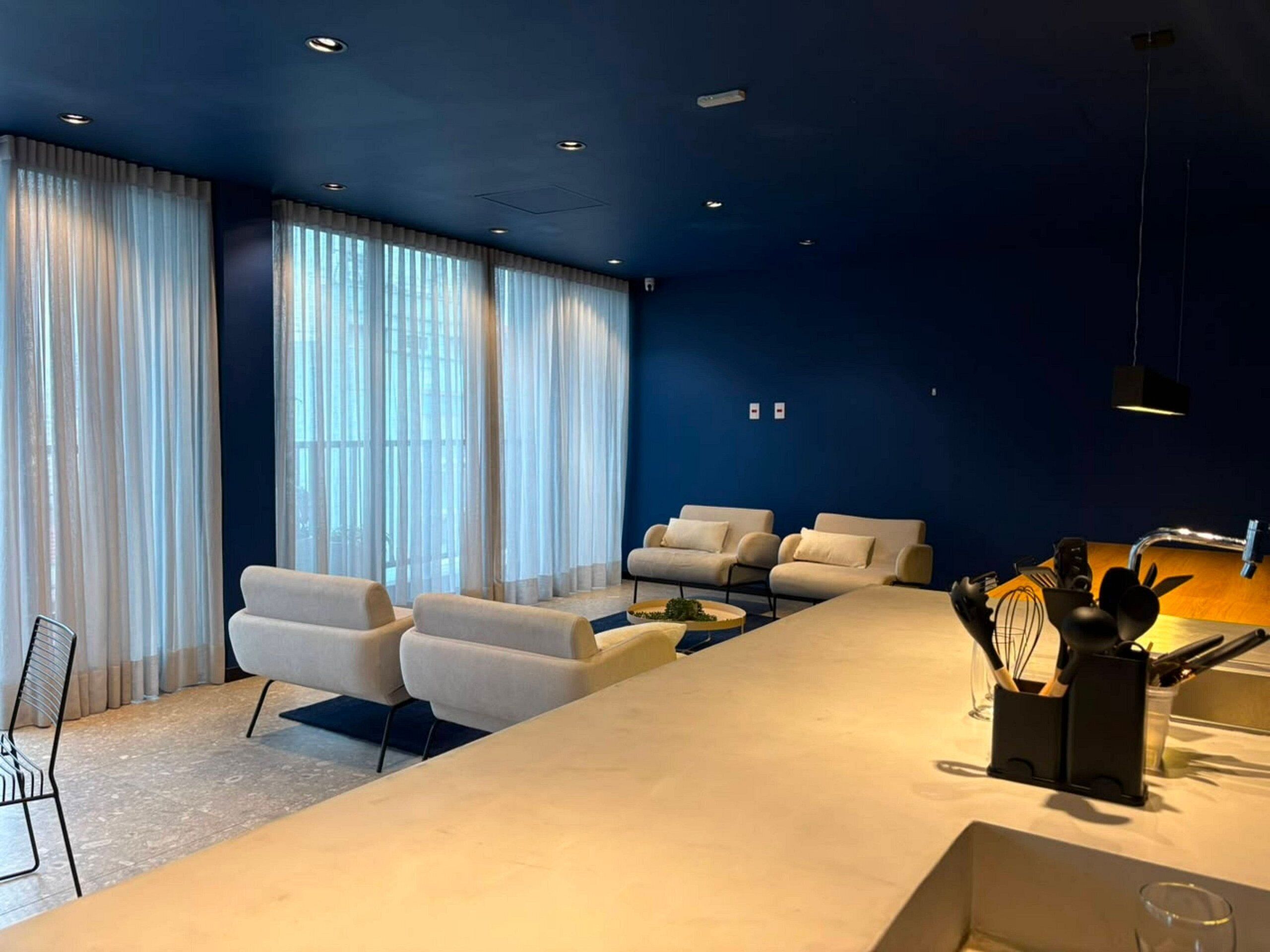 Una sala moderna con un sofá blanco largo, un sofá más pequeño y una mesa de centro. Hay una zona de cocina con un fregadero y utensilios.