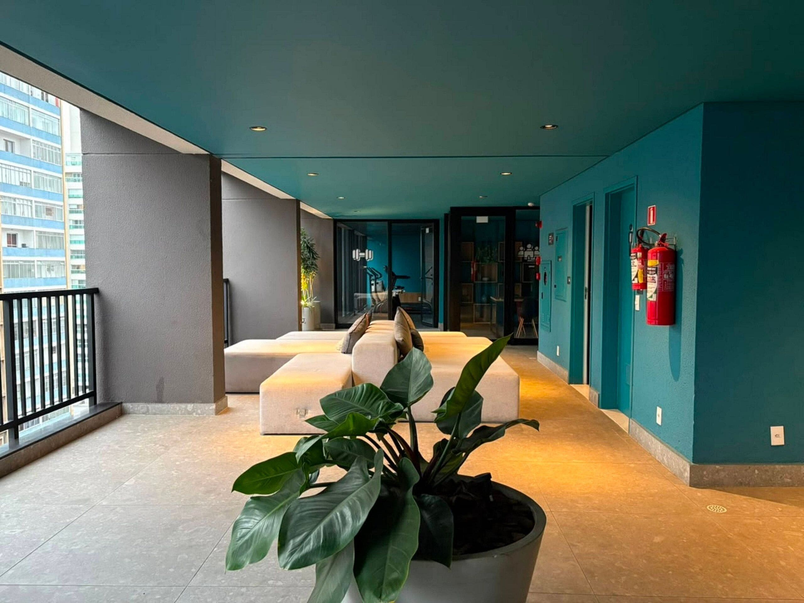 A modern interior with a teal accent wall, a seating area with a potted plant, and a fire extinguisher mounted on the wall.
