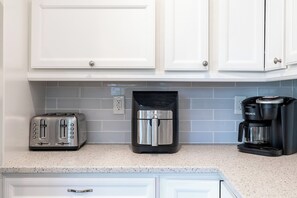 Eine Küche mit weißen Schränken, einem Toaster, einer Kaffeemaschine und einem schwarzen Gerät auf der Arbeitsfläche.