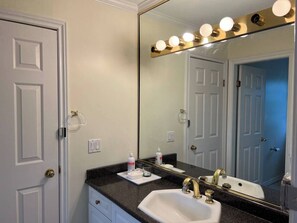 Un bagno con un lavandino bianco, uno specchio grande illuminato e una porta con maniglia in ottone.