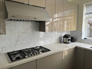A modern kitchen with a gas stove, a built-in oven, and a stainless steel range hood. - Two bedroom suite in a House/ 15 min YVR, AC (Richmond)
