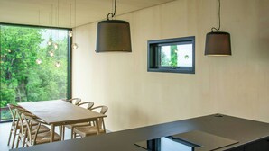 Et moderne køkken med en central ø, hængende lamper og et vindue med udsigt til grønne omgivelser.