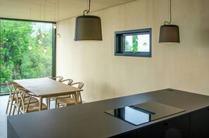 A modern kitchen with a central island, pendant lights, and a window overlooking greenery. - Architect-designed cabin with fjord views (Bryggja)