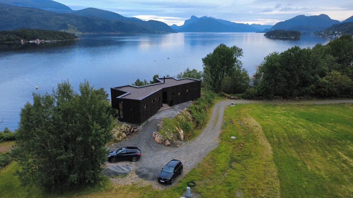 A modern building with a flat roof, surrounded by a grassy area and a body of water.