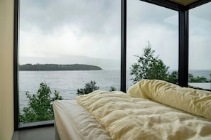 A bedroom with a large window overlooking a body of water and a distant island. - Architect-designed cabin with fjord views (Bryggja)