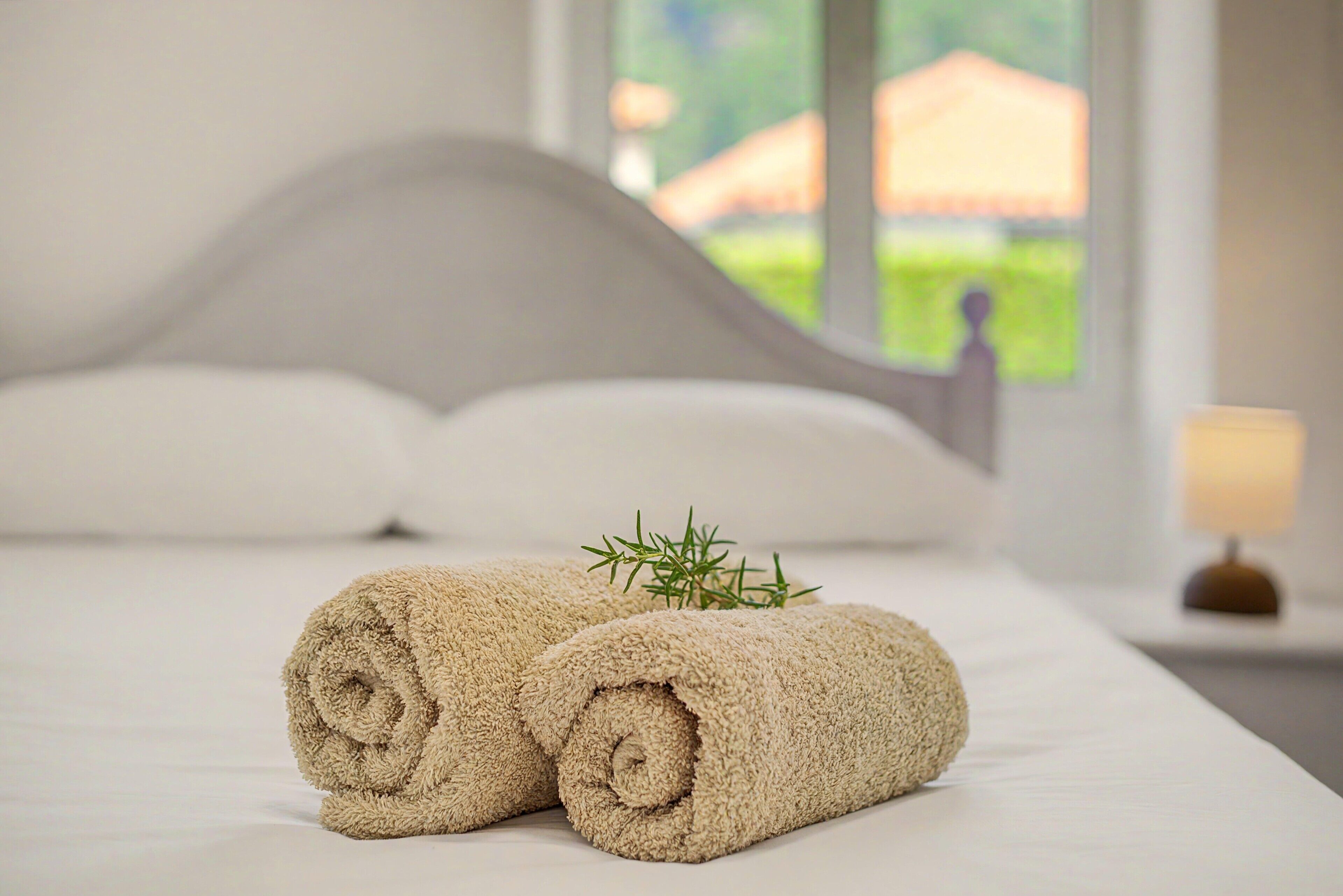 A neatly made bed with rolled towels and a sprig of rosemary on top.