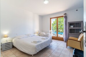 Ein Schlafzimmer mit Bett, Nachttisch, Lampe, Babybett, Sessel und Blick auf einen Außenpool.