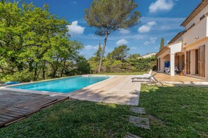 A swimming pool with a wooden deck, surrounded by lush greenery and a clear sky. - Écrin de verdure, charme provençal près de Cannes (Mouans-Sartoux)