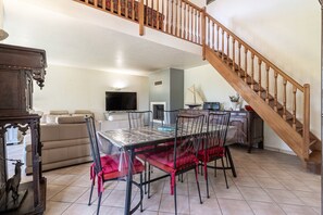 A dining area with a table and chairs, a sofa, a television, and a staircase. - Écrin de verdure, charme provençal près de Cannes (Mouans-Sartoux)