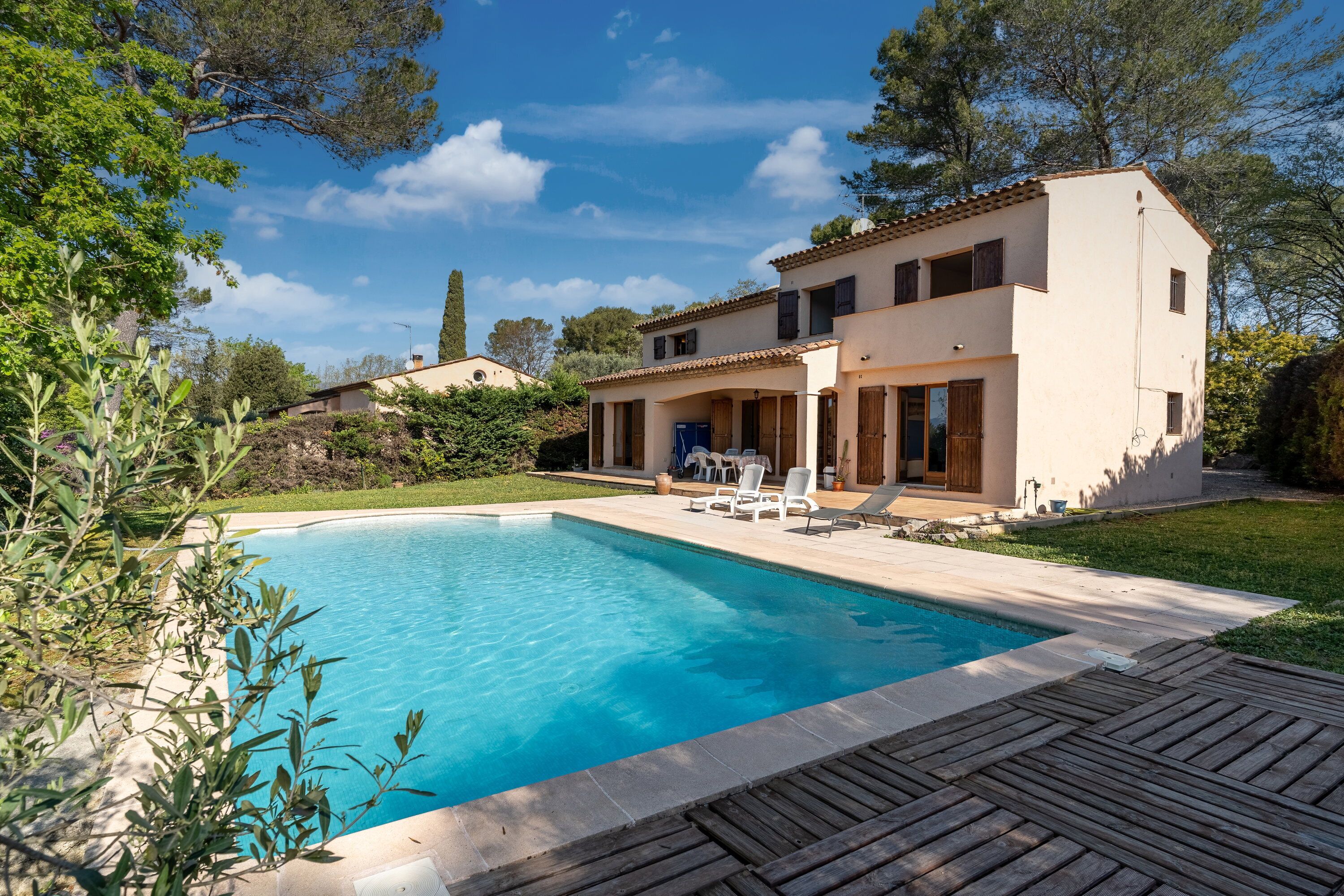 Une maison à deux étages avec une piscine, un patio doté de chaises longues et un jardin.