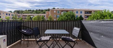 A terrace with a table and two chairs, a black chair with a cushion, and a white air conditioning unit.
